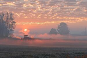 Tranquil misty sunrise over farmland with tractor in silhouette photo