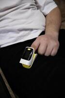 Man put on pulse oximeter on finger, check blood oxygen saturation. Monitoring heart rate at home. Vertical photo