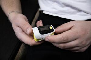 Man put on pulse oximeter on finger, check blood oxygen saturation. Monitoring heart rate at home photo