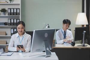 A woman and man sitting at a desk in front of a computer photo