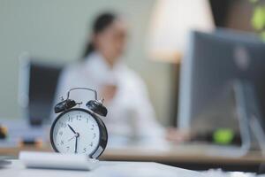 A clock on a desk in front of a woman photo