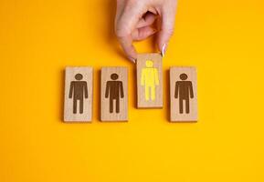 A hand selects a human figure from the options provided. Concept of talent search. Employee selection. Choosing the most suitable candidate for a role. Hiring, headhunting, corporate promotions. photo