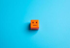 An orange cube with an amorphous, emotionless face. Apathy and indifference. The concept of the average person or consumer. Detachment, monotony and conformity. photo