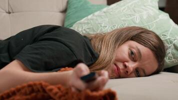 Woman lying on sofa holding remote control in hand and watching TV. Concept of rest, laziness and casual lifestyle video