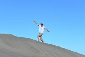 A man walking along a sand dune through barkhan in Maspalomas, Gran Canaria on a hot sunny day. A self confident man goes up the mountain - success and achievements concept photo