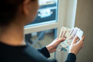 Counting cash in a well-lit room by a window, with emphasis on different banknotes and hand gestures, Ukrainian hryvnia photo