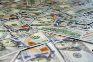 Stacks of hundred-dollar bills are spread out on a surface emphasizing the details of the new currency design side view in close up photo