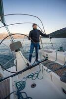 Young man captain standing at helm and controls a sailboat during a journey by sea in winter time in Montenegro photo