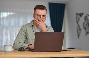A worried man using a laptop while working at home office. photo