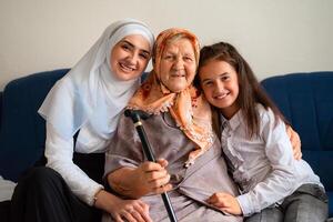 Portrait of muslim grandmother, mother and granddaughter hugging with love on the sofa smiling and looking at the camera. family of three female generations. photo