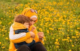 Happy Muslim family having fun mother and child boy playing together with dandelion in the flowering spring field. photo