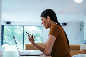 A woman sitting in the living room using a laptop and a smartphone look at camtalk by call with business friends and relatives, head shot. Job interview answering questions. photo
