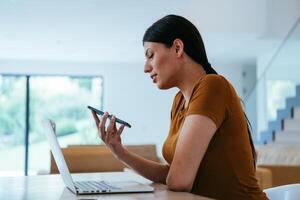 A woman sitting in the living room using a laptop and a smartphone look at camtalk by call with business friends and relatives, head shot. Job interview answering questions. photo