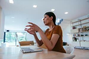 A woman sitting in the living room using a laptop and a smartphone look at camtalk by call with business friends and relatives, head shot. Job interview answering questions. photo