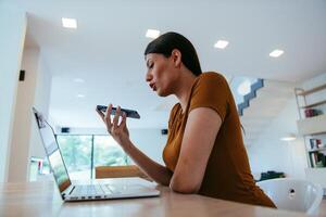 A woman sitting in the living room using a laptop and a smartphone look at camtalk by call with business friends and relatives, head shot. Job interview answering questions. photo