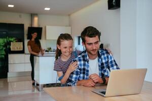 Work from home. Daughter interrupting her father while he is having a business online conversation on his laptop while sitting in the modern living room. photo