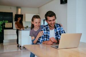 Work from home. Daughter interrupting her father while he is having a business online conversation on his laptop while sitting in the modern living room. photo