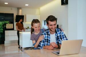 Work from home. Daughter interrupting her father while he is having a business online conversation on his laptop while sitting in the modern living room. photo