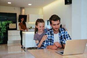Work from home. Daughter interrupting her father while he is having a business online conversation on his laptop while sitting in the modern living room. photo