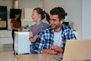 Work from home. Daughter interrupting her father while he is having a business online conversation on his laptop while sitting in the modern living room. photo