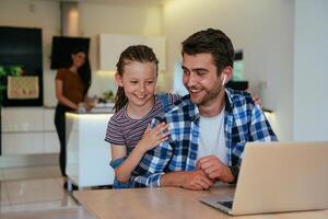 Work from home. Daughter interrupting her father while he is having a business online conversation on his laptop while sitting in the modern living room. photo