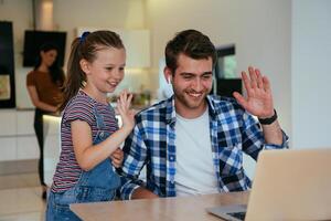 Work from home. Daughter interrupting her father while he is having a business online conversation on his laptop while sitting in the modern living room. photo