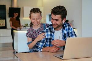 Work from home. Daughter interrupting her father while he is having a business online conversation on his laptop while sitting in the modern living room. photo