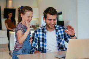 Work from home. Daughter interrupting her father while he is having a business online conversation on his laptop while sitting in the modern living room. photo
