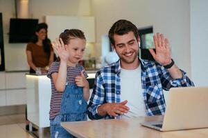 Work from home. Daughter interrupting her father while he is having a business online conversation on his laptop while sitting in the modern living room. photo