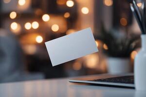 A blank business card hovers above a laptop keyboard in a sleek workspace. Soft lighting enhances the high-tech atmosphere, ideal for startups and digital branding photo