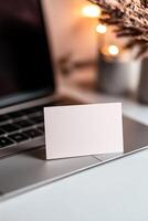 A blank business card floats gently above a laptop keyboard, surrounded by a sleek modern workspace. Soft light enhances the innovative atmosphere, perfect for startups photo