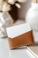 A blank business card is partially tucked into a fine-grain leather cardholder, with soft lighting reflecting its texture. The softly blurred background suggests a professional workspace photo