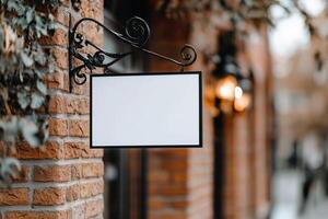 A blank rectangular signboard hangs from an ornate wrought iron bracket on a vintage brick wall, evoking a nostalgic atmosphere in a charming European street with warm lighting photo