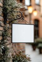 Rectangular signboard with a black metal frame is suspended from a decorative iron bracket on a vintage brick wall, creating a stylish backdrop in a quaint European street photo