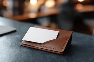 A blank business card is partially tucked into a fine-grain leather cardholder, reflecting soft lighting. The blurred backdrop suggests a sophisticated executive workspace, perfect for branding photo