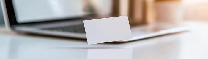 A blank business card hovers just above a sleek laptop keyboard, illuminated by soft lighting, in a high-tech workspace photo