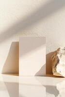 A blank business card is positioned upright against a neutral wall, gently leaning while reflecting softly on a smooth surface below. The aesthetic conveys professionalism and luxury photo