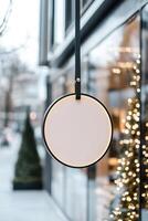 A round metal signboard is suspended from a minimalistic black bracket outside a chic boutique. The background features a high-end shopping street with glass reflections and soft-focus trees photo