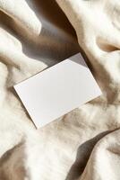 A blank business card rests on soft linen, with folds creating gentle shadows. The warm, neutral background enhances its texture, ideal for boutique or eco-friendly brand presentations photo