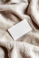 A blank business card rests on soft, textured linen, highlighting gentle folds and shadows. The warm background offers an earthy tone, ideal for eco-friendly branding and boutique aesthetics photo