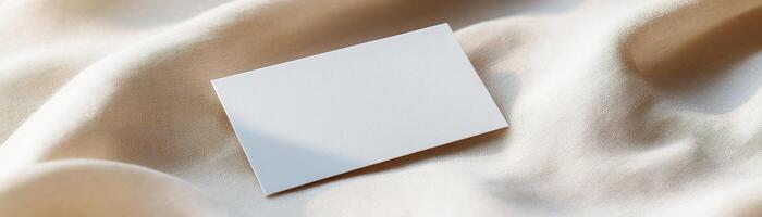 A blank business card rests on soft linen, showcasing subtle folds and shadows. The warm, earthy backdrop enhances its minimalist appeal, ideal for eco-friendly branding photo