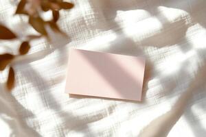 A blank business card lies flat on a smooth white surface, illuminated by soft natural light that creates subtle shadows, emphasizing the card's clean design for professional use photo