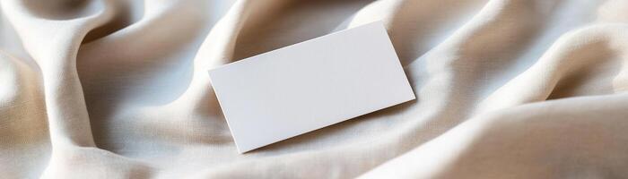 A blank business card rests on soft, wrinkled linen, casting delicate shadows, and surrounded by a softly blurred, warm background conveying a refined and natural atmosphere photo