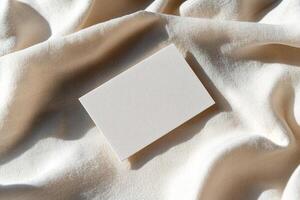 A blank business card is placed on gently wrinkled linen fabric, creating soft shadows. The warm earthy backdrop enhances the natural, refined aesthetic, ideal for eco-friendly brands photo