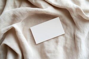 A blank business card rests on soft linen fabric, highlighting subtle folds and shadows. The neutral earthy background enhances warmth, ideal for eco-friendly and boutique branding photo