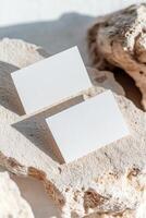 Two blank business cards rest on a textured stone surface, highlighted by sharp shadows that enhance the minimal aesthetic. The softly blurred background complements the contemporary look photo