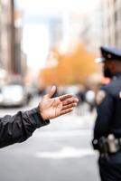 A police officer in uniform gestures to a civilian while providing assistance on a busy city street. Urban buildings and traffic create a lively background supporting public safety photo