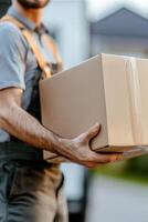 A professional mover wearing a uniform is carrying a labeled cardboard box while standing close to a moving truck. Suburban homes are softly blurred in the background, creating a friendly atmosphere photo