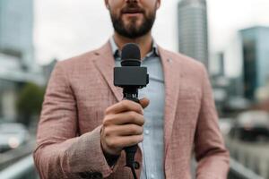 A news reporter in a stylish suit delivers a confident segment in front of a camera. The blurred city skyline and traffic create a vibrant backdrop, emphasizing the media's fast-paced nature photo