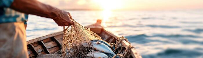 A seasoned fisherman on a wooden boat draws a net brimming with fresh fish as the sun rises, casting soft light over the tranquil ocean and distant shore photo